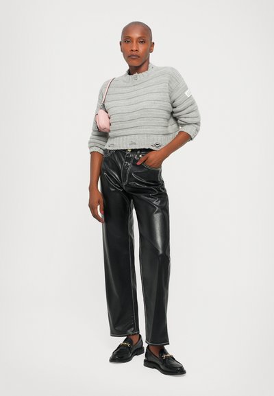 Grå stickad kort tröja med ribbad textur, ihop med svarta byxor i konstläder med breda ben. Modellen bär svarta loafers och håller en rosa väska.