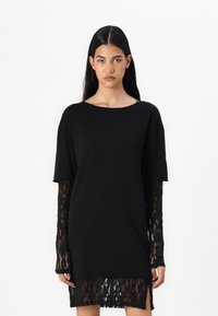 A fekete ruha rövid, laza fit, csipkebetétes hosszú ujjakkal, kerek kivágással és csipke díszítéssel a szegélyen. Puha anyag, textúrált felülettel.