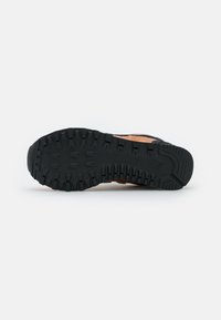 Suela de goma negra de un zapato de piel marrón con surcos profundos y patrones de textura para un mejor agarre, exhibida sobre un fondo blanco.