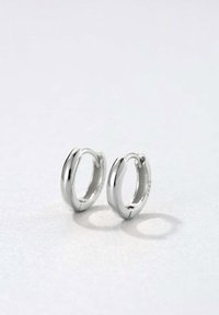 Srebrne kolczyki w kształcie obręczy o gładkim, zaokrąglonym wzornictwie i polerowanym wykończeniu, z bezszwowym zapięciem i minimalistyczną formą.