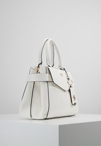 Valkoinen teksturoitu käsilaukku mustilla yksityiskohdilla, kahdella pääkahvalla ja kultaisella metallisella yksityiskohdalla. Sisältää läppäkiinnityksen ja pendanttikoristeen.