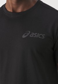 Camiseta negra de manga corta confeccionada en una tela suave, con un sutil logo negro de "asics" en el frente y un cuello redondo.