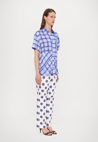 Camicetta a maniche corte a quadretti nelle tonalità di blu, abbinata a pantaloni bianchi con grandi pois viola. Tacchi neri eleganti completano l'outfit.