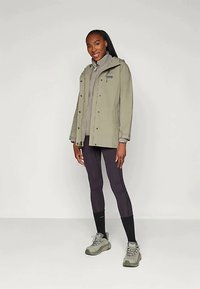 Svetlozelená nepremokavá bunda, šedý fleecový interiér, čierne legíny a šedé turistické topánky. Jednoduchý dizajn bez viditeľných vzorov alebo akcentov.