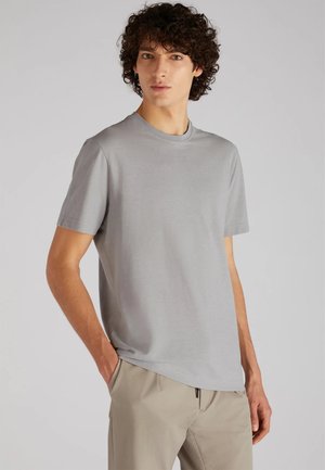 Camiseta gris de manga corta hecha de una tela suave, con un corte clásico y un ajuste relajado, combinada con pantalones claros de textura.