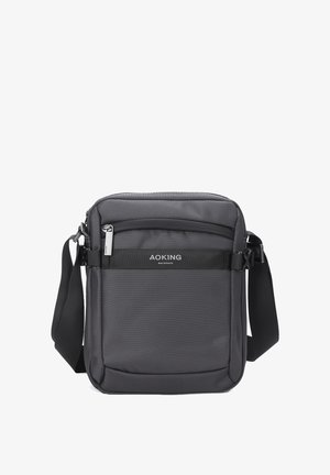 Schwarze Umhängetasche mit strukturiertem Oberflächen, mit Reißverschlussfächern, verstellbarem Tragegurt und einem Logolabel auf der Vorderseite. Kompakte rechteckige Form.