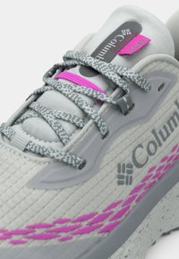Γκρι αθλητικό παπούτσι με υφή στην επάνω επιφάνεια, ροζ λεπτομέρειες και γκρι κορδόνια. Διαθέτει λογότυπο στο πλάι και επενδυμένη σόλα.