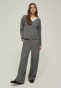 Felpa grigia con scollo a V e colletto bianco, abbinata a pantaloni grigi a gamba larga. Tessuto morbido con una vestibilità rilassata. Scarpe nere completano l'outfit.