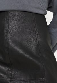 Svart läderkjol med en strukturerad yta och synliga veck, en figurnära design och en söm som löper vertikalt för extra detaljer.