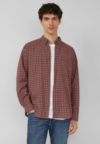 Kariertes Hemd zum Knöpfen in Kastanienbraun und Creme, mit langen Ärmeln, Kragen und einer einzelnen Brusttasche. Darunter ein weißes T-Shirt getragen.