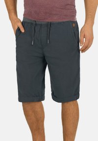 Shorts en coton gris foncé avec une taille à cordon, poches latérales et ourlets rollés. Présente un petit patch logo à l'avant.