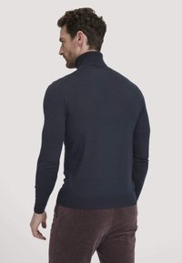 Marineblauwe hoge hals trui van gebreide stof, aansluitend model, lange mouwen, geribbeld kraag en zoom, gedragen met bruine ribfluwelen broek.