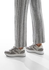 Scarpe da ginnastica grigie con una combinazione di suede e mesh nella parte superiore, suola bianca e rivestimenti morbidi. Abbinati a pantaloni larghi grigi a coste.