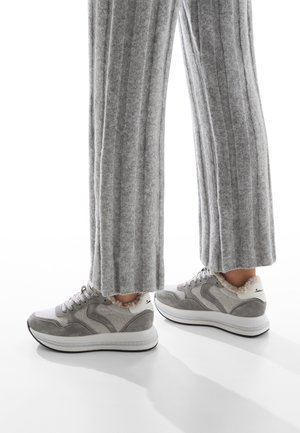 Scarpe da ginnastica grigie con una combinazione di suede e mesh nella parte superiore, suola bianca e rivestimenti morbidi. Abbinati a pantaloni larghi grigi a coste.