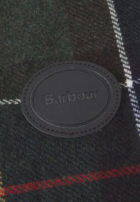 Tartan vlněná deka s tmavě zeleným a černým vzorem, s černou koženou etiketou s embosovaným nápisem "Barbour." Prošité okraje.