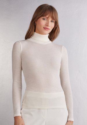 Top de cuello alto acanalado en crema claro, con mangas largas y silueta ajustada. Textura suave con una banda ligeramente más clara en el dobladillo.