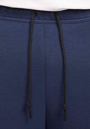 Pantalones de chándal azul marino con una textura suave, cinturilla elástica y cordones negros asegurados con puntas de plástico. Sin patrones visibles.