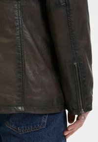 Braune Lederjacke mit einem Reißverschluss an den Manschetten. Die Textur ist glatt und weist kontrastierende Nähte entlang der Säume sowie eine taillierte Passform auf.