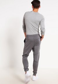 Grå långärmad tröja kombinerad med mörkgrå joggers med sidfickor och avslappnad passform. Fotsättningen är vita sneakers.