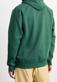 Vihreä hupullinen collegepaita, joka on valmistettu pehmeästä kankaasta; siinä on rento istuvuus, resorireunaiset hihansuut ja kuminauhavyötärö. Yksinkertainen design ilman näkyviä logoja.