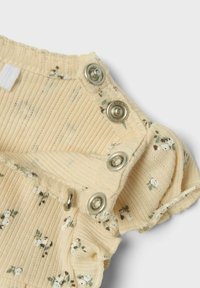 Gul ribbad jumpsuit i tyg med blommönster, med silverfärgade tryckknappar och volangkantade ärmar, texturerad och mjuk.