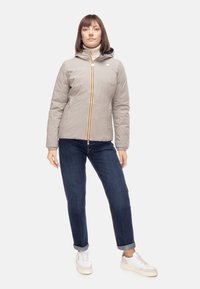 Giacca imbottita grigio chiaro con cappuccio, dotata di una cerniera verticale gialla e rossa. Abbinata a jeans blu scuro e scarpe da ginnastica bianche.