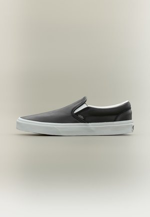 Zwarte slip-on Vans-schoen met witte rubberen zool en klein logolabel, weergegeven in profiel op een neutrale achtergrond.