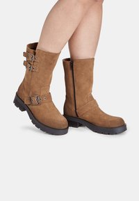 Pruun nahast pahkluu saapad, millel on lame kummist tald, kaks reguleeritavat pandla rihma ning külgsiibra, mis tagab mugava jalga panemise.