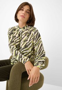 Langsleeve blouse van lichtgewicht, doorzichtig materiaal met een abstract patroon van groene en bruine zebraprinten. Hoge kraag met geplooide details.