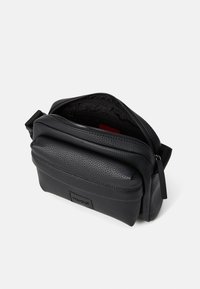 Borsa a tracolla in pelle nera con finitura testurizzata. Presenta un ampio scomparto con zip e una piccola tasca frontale, logo del brand sul davanti.
