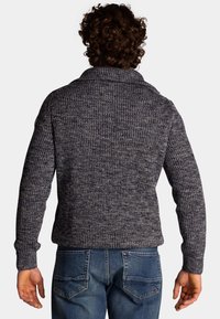 Gebreide trui in donkerblauwe en grijze tinten, met een geribbelde textuur, oversized kraag en lange mouwen. Gemaakt met blauwe denim jeans.