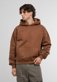 Hnědá mikina s klokaní kapsou, oversized střih, kapuce na šňůrku a žebrované manžety; spojená s cargo kalhotami. Měkká textilie.