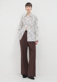 Camicia bianca con righe nere verticali, stile con bottoni, abbinata a pantaloni marroni larghi. Tessuto morbido, vestibilità comoda.