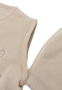 Top sans manches beige avec tissu texturé. Présente un col rond et des bords cousus. La surface a une apparence douce et subtile.