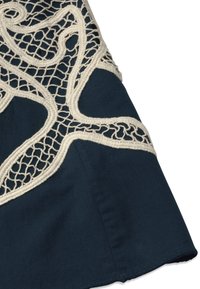 Tissu bleu marine avec une broderie en dentelle beige complexe formant des motifs abstraits et fluides sur un bord du textile.