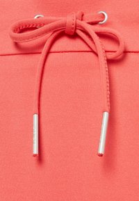 Cintura de joggers color coral con cuerda interior. Textura suave con extremos de los cordones en metal plateado.