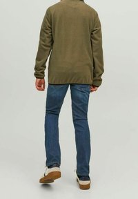 Olivgrön fleecejacka med avslappnad passform, tillsammans med blå denimbyxor och vita sneakers med bruna gummisålar.