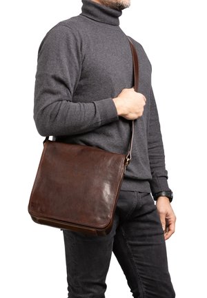 Borsa a tracolla in pelle marrone con una superficie liscia, forma rettangolare, tracolla regolabile e chiusura con zip, indossata sulla spalla.