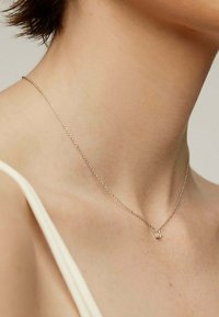 Collar de cadena de plata con un pequeño colgante geométrico. Textura suave con un acabado pulido, llevado ajustado alrededor del cuello.