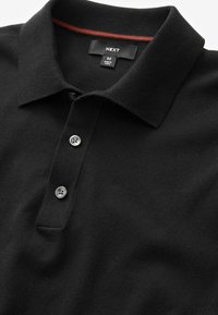 Sort polo skjorte lavet af strikstof, med en klassisk krave, tre knaplukninger og en diskret rød detalje på indersiden af kraven.