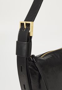 Black leather shoulder bag featuring a textured finish, gold hardware, and a wide adjustable strap with a buckle detail.