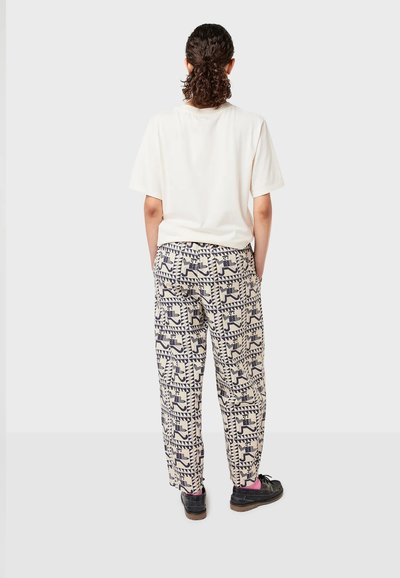Loose-fitting patterned pants in cream with navy geometric designs, paired with a plain white T-shirt, worn with black shoes.