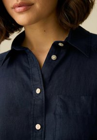 Marineblauwe knoopshirt van lichtgewicht stof met een gestructureerde kraag, met kunststof knopen en een borstzak links.