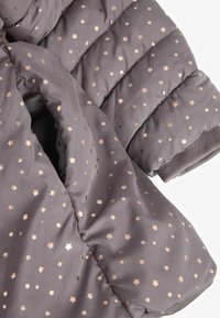 Manche et partie avant d'une veste matelassée gris foncé avec des motifs d'étoiles métalliques dorées et argentées et un bord-côte à la manche.