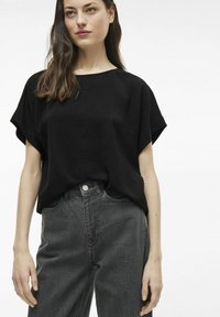 Juodas tekstūruotas trumpas marškinėliai, derinami su pilkais džinsiniais kelnėmis, turinčiomis aukštą juosmenį, mygtuko uždarymu ir šoninėmis kišenėmis.