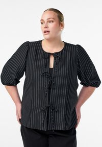 Črna prugasta bluzica s kratkimi napihnjenimi rokavi, ki ima okroglo ovratnico in sprednje zapiranje na zavezo. Narejena je iz lahkotnega blaga z gladko teksturo.