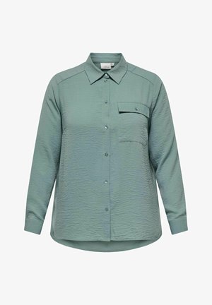 Zelena zgužvana tkanina srajca z dolgimi rokavi, s koničastim ovratnikom, sprednjim gumbom in enim žepom na prsih. Okrogel rob na dnu.