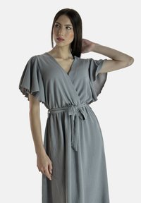 Robe enveloppante grise avec des manches courtes et volantées, un décolleté en V et une ceinture nouée à la taille. Fabriquée en tissu léger et texturé.