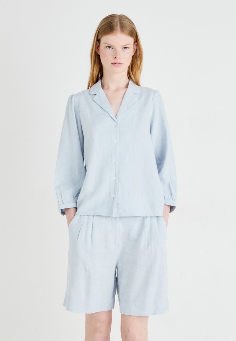 Completo due pezzi in lino azzurro chiaro, composto da una camicia a maniche lunghe con colletto e pantaloni corti a vita elastica con una vestibilità comoda.