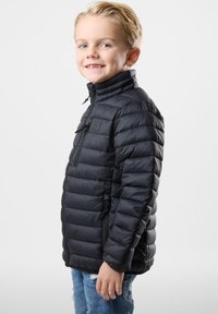 Sort pufferjakke med høj krave, lynlåslommer og ribbede manchetter, der har et quiltet design og en glat tekstur.